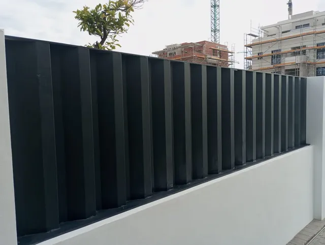 Cerramiento de lamas verticales negras sobre muro de parcela