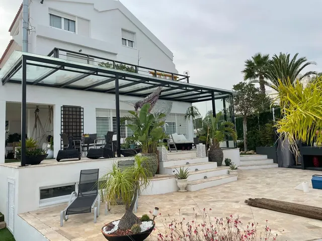Porche con estructura metálica negra y techo de cristal sobre una terraza